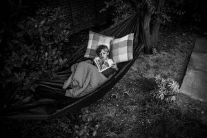 young boy relaxing ina. hammock and reading a book during the school summer holidays