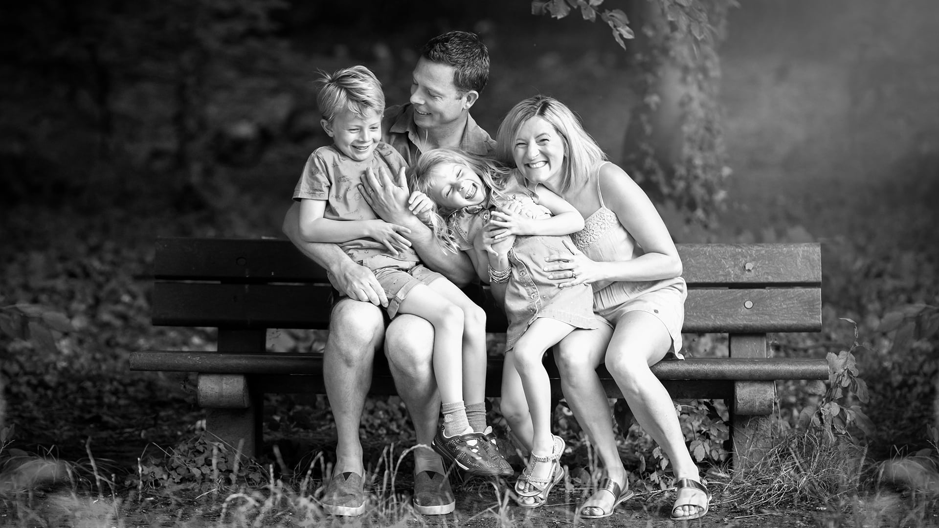 family giggling ona. park bench in Cambridge during a photoshoot