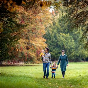 family walking through autumn trees during a photoshoot at wandlebury country park in cambridgeshire