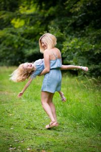 little girl being swung playfully by her mother during a family photoshoot in Lode, Cambridgeshire