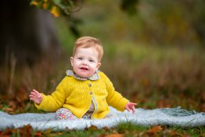 baby girl sitting on a rug in autumn leaves during a family photo shoot in cambridgeshire