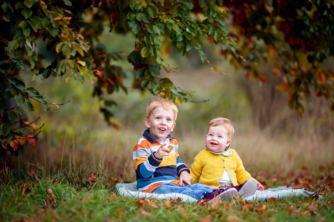 young siblings playing with leaves at Wandlebury Country park in Cambridge